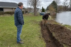 Husägare tittar på när en arbetare gräver dike vid tomtgränsen under ett projekt för att renovera gammalt hus.